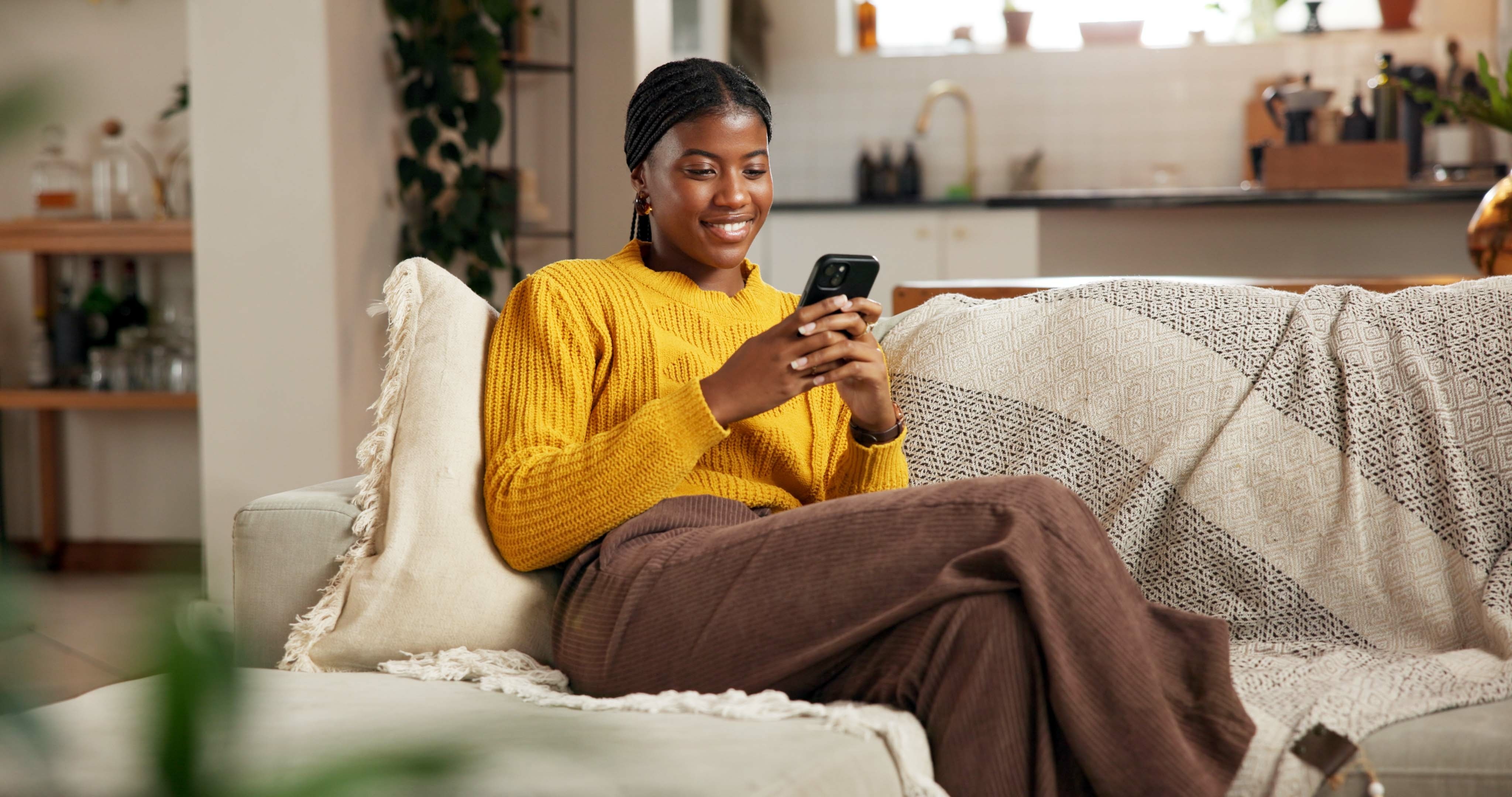 Une femme consulte son téléphone depuis son canapé.