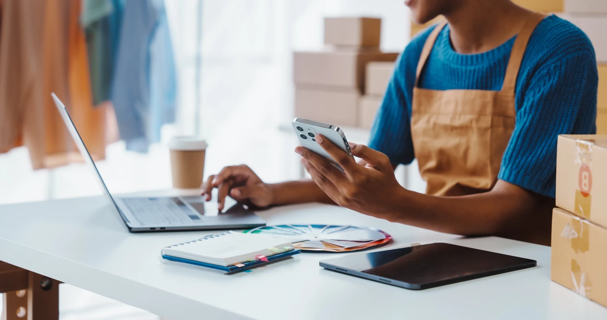 Une entrepreneuse gère ses commandes depuis son téléphone et son ordinateur.